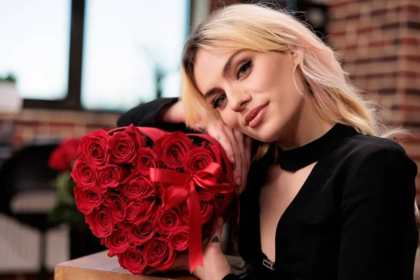 Blonde woman posing with red roses, looking at camera close up, valentines day luxury present. Attractive blonde girlfriend with gift from boyfriend, love holiday greeting, flowers delivery service