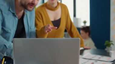 Colleagues in startup office talking about marketing strategy looking at laptop screen standing at desk. Coworkers doing teamwork working on business action plan using portable computer.