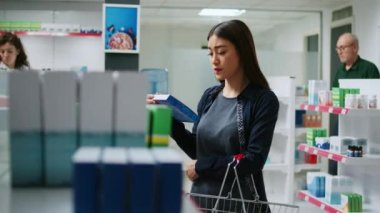 Asyalı müşteri ilaç kutularına ve raflardaki ilaç şişelerine bakıyor, ilaç ve ilaç almak için eczacıları kontrol ediyor. İlaç paketi broşürü okuyan kadın.
