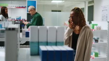 Afro-Amerikalı mutlu müşteri eczane raflarındaki ilaç paketlerini kontrol ediyor, eczanedeki kutularda sağlık ürünleri ve vitaminler alıyor. Hap ve uyuşturucuya bakan kişi.