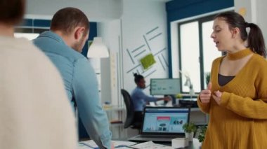 Man in startup office zoomin in digital tablet using touchscreen presenting sales charts to woman colleague standing next to desk. Team of two coworkers working on group marketing project.