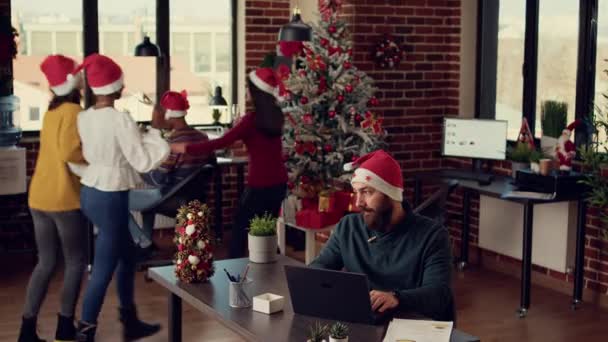 紧张的男人被快乐的同事们打断了 他们用圣诞装饰品庆祝办公室里的寒假 圣诞节前夕 吵吵闹闹的人在骚扰人 — 图库视频影像
