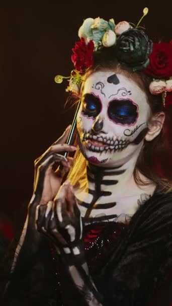 垂直ビデオ 死んだ女性がスマートフォンで電話で話して 花冠とカヴァレラのカトリーナハロウィンの衣装を着ています メキシコ文化の休日を祝うためにサンタのマウスとして身に着けている女性 — ストック動画
