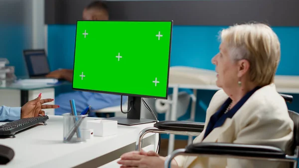 Patient with chronic impairment looking at greenscreen on monitor, analyzing isolated display with chroma key background at checkup. Woman in wheelchair using mockup copyspace template.