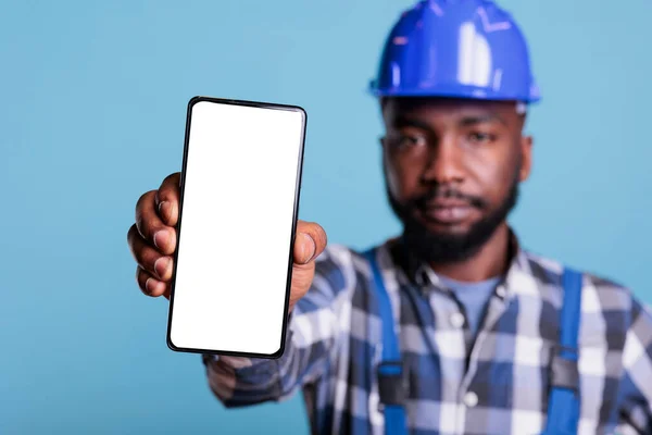 白い画面で現代的な携帯電話を示す深刻な建設労働者は 広告のモックアップ アフリカ系アメリカ人のビルダーは アプリケーションのプロモーションのための空のディスプレイと電話を保持 — ストック写真