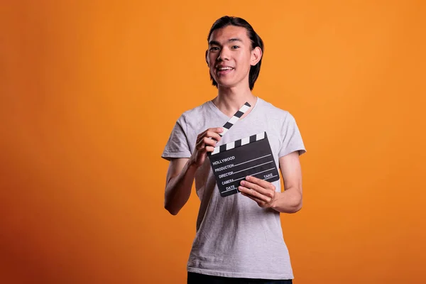 Cameraman assistant holding film making clapperboard, movie scene shooting. Cinematography, filmmaking, video production, young smiling asian clapper loader slapping slate