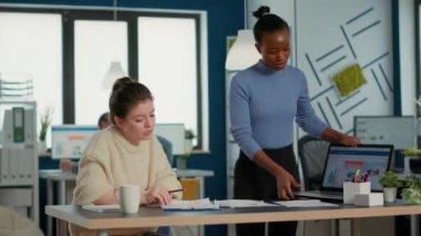 Afrika kökenli Amerikalı girişimci iş arkadaşının yanında duruyor dizüstü bilgisayardaki pazarlama stratejisini çizelge ve istatistiklerle sunuyor. İş piyasası payını analiz eden grup projesinde çalışan meslektaşlar.