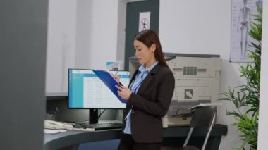 Asyalı resepsiyonist bilgisayardaki randevu listesini kontrol ediyor ve hastane resepsiyonundaki raporlar üzerinde çalışıyor. Sağlık çalışanı formlara yardım ediyor, sağlık merkezinde sigorta desteği veriyor..
