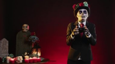 Stüdyoda video oyunları oynayan, oyun konsolunda oynamak için kumanda kullanan kadın. Ölü geleneğinin Meksika Günü 'nden kalma ürkütücü Cadılar Bayramı kostümü giyiyor..