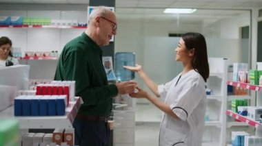 Asyalı eczacı çeşitli hastalarla konuşuyor, eczane raflarından ilaç ürünleri veriyor. Çalışanlar insanlara tıbbi yardım yapıyor, eczanedeki ilaçları açıklıyor..