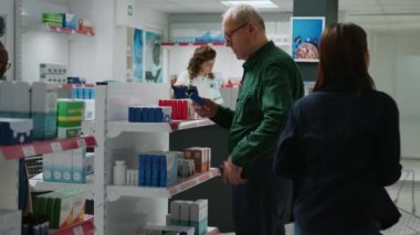 Eczane raflarından ilaç ve sağlık tedavisi almak için ilaç kutuları alan kıdemli adam eczacıyla eczacılık ürünleri hakkında konuştu. İlaçlar ve ilaçlar satın alınıyor..