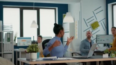 Smiling successful employee with great work results receiving congratulations from coworkers at desk. Woman working on laptop happy with business turnover celebrates with team in startup office.