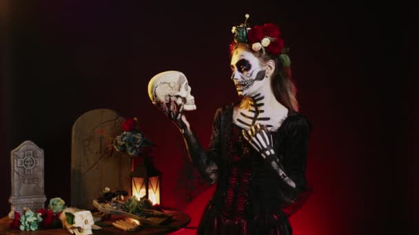 若い怖いモデルは スタジオで頭蓋骨とポーズ メキシコのハロウィンのDios Los Muertosで不気味な演技 伝統文化を祝うためにラ カヴァレラ カトリーナのように見える薄汚い女性 — ストック動画