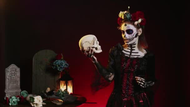 ハロウィーンの頭蓋骨を見て 手に頭蓋骨で不気味な行動をする不気味な女性 怖いメイクを身に着けていることは神聖なメキシコの儀式に花冠とボディアートとサンタのマテのように見えます — ストック動画