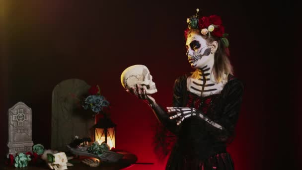 在工作室里拿着神圣骷髅的可怕的死去的女人 在庆祝墨西哥光棍节的时候表现得既可怕又恐怖 华丽的女神 身穿带有身体艺术的节日服装 看起来像死亡之女 — 图库视频影像