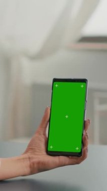Dikey video: Kafkas kadın sahte yeşil ekran krom anahtar telefon kullanarak çevrimiçi video görüşmesi yapıyor. İnternet uygulamasında çalışan iş kadını, ofisteki ofis masasında izole bir cihaz kullanıyor.