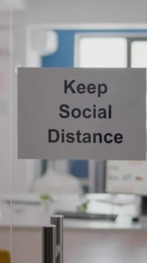 Duvarında sosyal mesafe tabelası olan dikey video işi cam ofis. Küresel salgın ve koronavirüs krizi sırasında içinde kimse olmayan modern ofis alanı