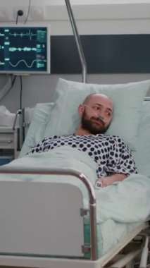 Dikey video: Uzman doktor siyahi kadın doktor hastane koğuşunda tablet bilgisayar kullanarak X-ray 'i gösteriyor. Hasta hasta hasta iyileşme sürecinde yatakta oturuyor.