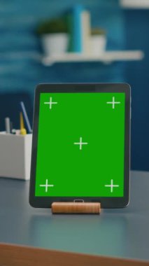 Dikey video: Bir kadın, ofis masasında oturan yeşil ekran krom anahtarıyla tablet bilgisayara bakarken bir fincan kahve içiyor. İnternet için izole edilmiş aygıt kullanan serbest çalışan