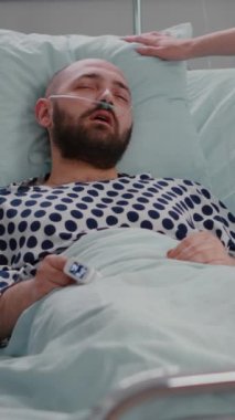 Dikey video: Hastane koğuşundaki iyileşme randevusu sırasında Sıcaklığı kontrol eden hemşire. Hasta hasta yatakta dinlenirken, rehabilitasyon asistanı...