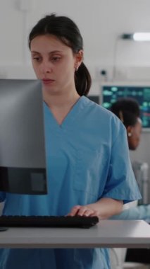 Dikey video: Arka planda siyahi pratisyen hekimlerin hasta adam sağlığı tedavisi ile ilgili tartışırken hemşirelerin bilgisayarda tıbbi uzmanlık yazarken ön görünümü. Hastanede yatan hasta...
