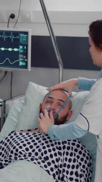垂直ビデオ アフリカ系アメリカ人医師がクリップボード上で症状の病気を書いて病気の男性と議論しながら 女性の医療酸素マスクを入れて呼吸器疾患を監視します 入院中の患者さん — ストック動画