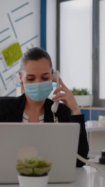 Koruyucu yüz maskeli dikey video girişimcisi sabit hatta otururken bilgisayarın başında konuşuyor. Beyaz kadın Coronavirus sırasında iş toplantısında çalışıyor.