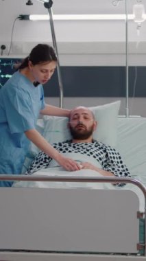 Dikey video: Hastalık tedavisi sırasında hastayı izleyen pratisyen hemşire hastane koğuşunda çalışan panoya hastalık belirtileri yazıyor. Hastanedeki hasta adamın solunum sorunu var.