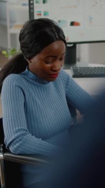 Video dikey: Engelli, engelli, kameraya bakıp gülümseyen, iş yerindeki ofis odasında oturan ve mali projede ekiple birlikte çalışan Afrikalı kadın. İş kadını.