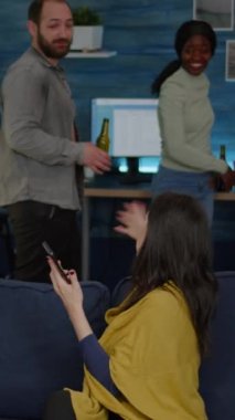 Dikey video: Çok ırklı arkadaşlar birlikte takılır, sosyalleşirken akıllı telefondan komik videolar izlerler. Bir grup çok ırklı insan gecenin geç saatlerinde kanepede oturup bira içiyor.