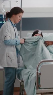 Dikey video: Hastane koğuşunda kalp atışı nabzını kontrol eden hasta bir kadının acil durum sırasında yatağa yatmasına yardım eden tıbbi ekip. Hastanın solunum yolu var.