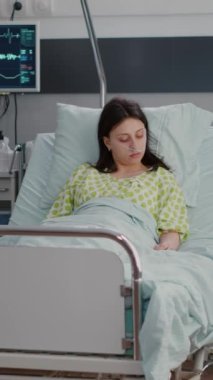 Dikey video: Afro-amerikan asistanı, hastane koğuşunda hastalık tedavisi sırasında hasta kadın yatağı ayarladı, pratisyen doktor hasta analizi yapıyor, iyileşme sürecini açıklıyor.