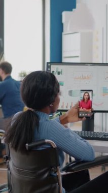 Video dikey: Engelli Afrikalı çalışan felçli, tekerlekli sandalyede oturan kulaklıkları kullanarak uzaktan kumandalı telefondaki yöneticiye finansal raporları açıklıyor. başlat
