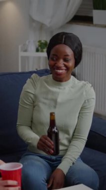 Dikey video: Siyah tenli kadın gece geç saatlerde arkadaşlarıyla oturma odasında toplanıyor ve bira içerken yaşam tarzı tavsiyelerini paylaşıyor. Bir grup melez insan vakit geçirmekten zevk alıyor.