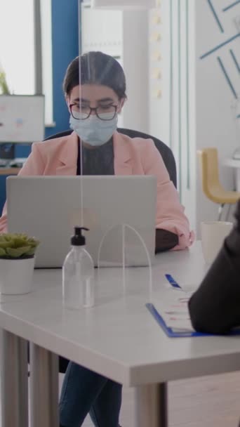 垂直ビデオフリーランサーは コロナウイルスの感染を防ぐために保護面を身に着けている新しい通常のオフィスに座っている間 ビジネス戦略について同僚と話しています 社会を尊重するチーム — ストック動画