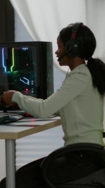 Dikey video: Kazanan siyah oyuncu oyun sandalyesinde oturuyor ve kablosuz kontrolörle video oyunları oynuyor. Profesyonel siber adam RGB 'deki esport turnuvası için online video oyunları yayınlıyor.
