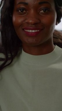 Dikey video: Siyahi kadın oyuncu kameraya bakıyor, gülümsüyor ve sanal ortamda sanal atıcılık oyunu şampiyonluğu oynuyor, esportcular oyun sırasında şık bir bilgisayarda güçlü bir performans sergiliyorlar.