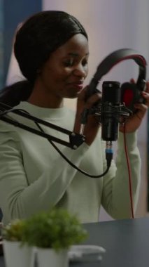 Dikey video: Afrikalı blogcu podcast çekerken seyirciye gülümsüyor, kulaklık takan kameraya bakıyor. Canlı yayın yapan internet yayın sunucusu dijital kayıt yapıyor.