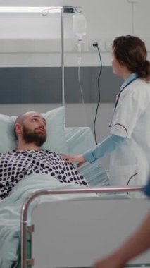 Dikey video: Hastane koğuşunda solunum uzmanlığı sırasında kalp atışlarını analiz eden terapist doktor. Hasta hastayı tekerlekli sandalyeye mahkum eden hemşire bacağının ardından iyileşme sürecinde olan bir fizyoterapi uzmanı.