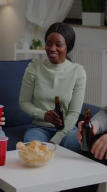 Dikey video: Çok ırklı arkadaşlar birlikte vakit geçirir, gece partisinde bira içerken gece geç saatlerde oturma odasında kanepede otururlar. Bir grup melez insan takılıyorlar, eğleniyorlar.