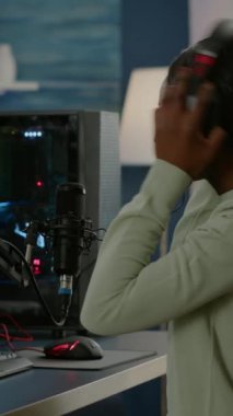 Dikey video: Profesyonel e-spor afro oyuncu canlı turnuva sırasında mikrofonla konuşuyor. Çevrimiçi şampiyonluk sırasında kulaklık takmak ve klavyede yazmak için viral video oyunları.