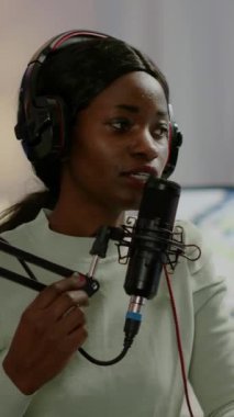 Dikey video: Online programın Afrikalı kadın sunucusu mikrofona kulaklık takarak konuşuyor. Canlı yayın sırasında konuşan, internette konuşan, kulaklık takan, canlı yayın yapan bir blog yazarı.