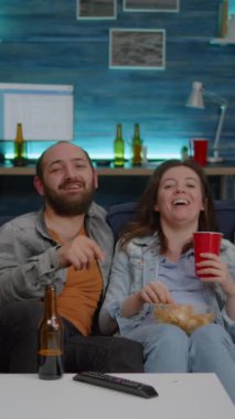 Dikey video: Çoklu etnik arkadaşlar gülerken komedi filmi seyrediyorlar ve birlikte vakit geçiriyorlar. Heyecanlı bir grup insan abur cubur yiyor, bira içiyor ve gece geç saatlerde eğleniyorlar.