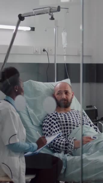垂直ビデオ 医療チームは 病院病棟で寛解療法のためにドリップバッグに流体を注入する患者のバイタルチェック心拍数を監視します 診療中に医療を待っている病気の女性 — ストック動画