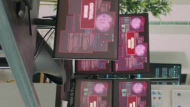 Dikey video: Ekranda hata mesajı gösteren birden fazla monitörlü masa, hacklenen bilgisayar sunucusu. Sistem hatası güvenliği ve hackleme uyarısı olan boş yazılım geliştirme bürosu.