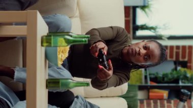 Dikey video: Birlikte oyun oynayan çok ırklı arkadaş grubu, TV konsolunda oyun yarışması. Bira şişeleri ve abur cuburlarla sosyal toplantının tadını çıkarıyorum, eğleniyorum.