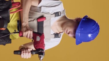 Dikey video: Güçlü tamirci kadın çivi çakmak için elektrikli matkap tabancası kullanıyor, inşaat onarımı için elektrikli matkap makinesiyle çalışıyor. Mühendislik projesi üzerine mimari yeniden inşa