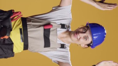 Dikey video: Güçlü tamirci kadın yukarı yönde reklam vermek ve inşaat inşaatında çalışmak için yukarı işaret ediyor. Müteahhit, yukarıdaki stüdyoda ve mühendislik üniformasında reklam olduğunu belirtiyor..