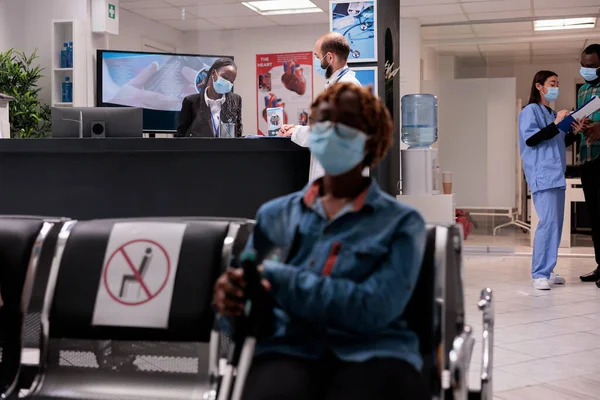 African american woman on crutches waiting to be seen in medical tower. Asian female doctor showing results to patient. Healthcare professional reviewing emergencies with curly haired receptionist.