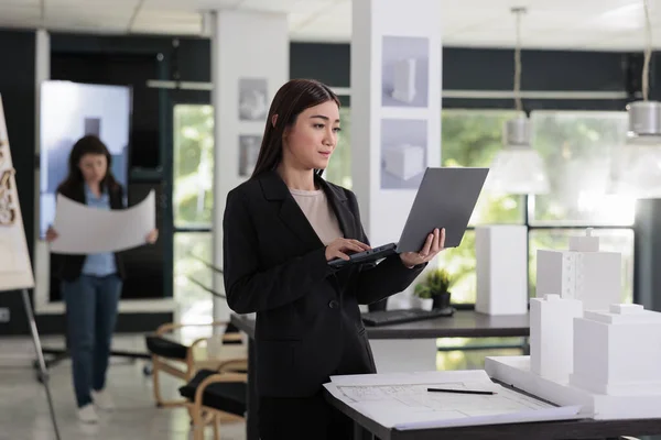 Architect modeling 3d building, using software on laptop, working with city construction project in architecture office. Employee engineering, real estate worker standing with computer